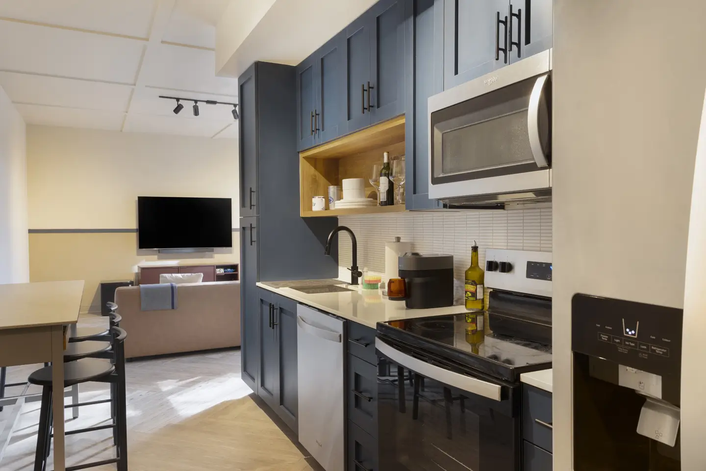 Fully furnished kitchen with oven, microwave, fridge, dishwasher - and in the distance is a couch and TV.
